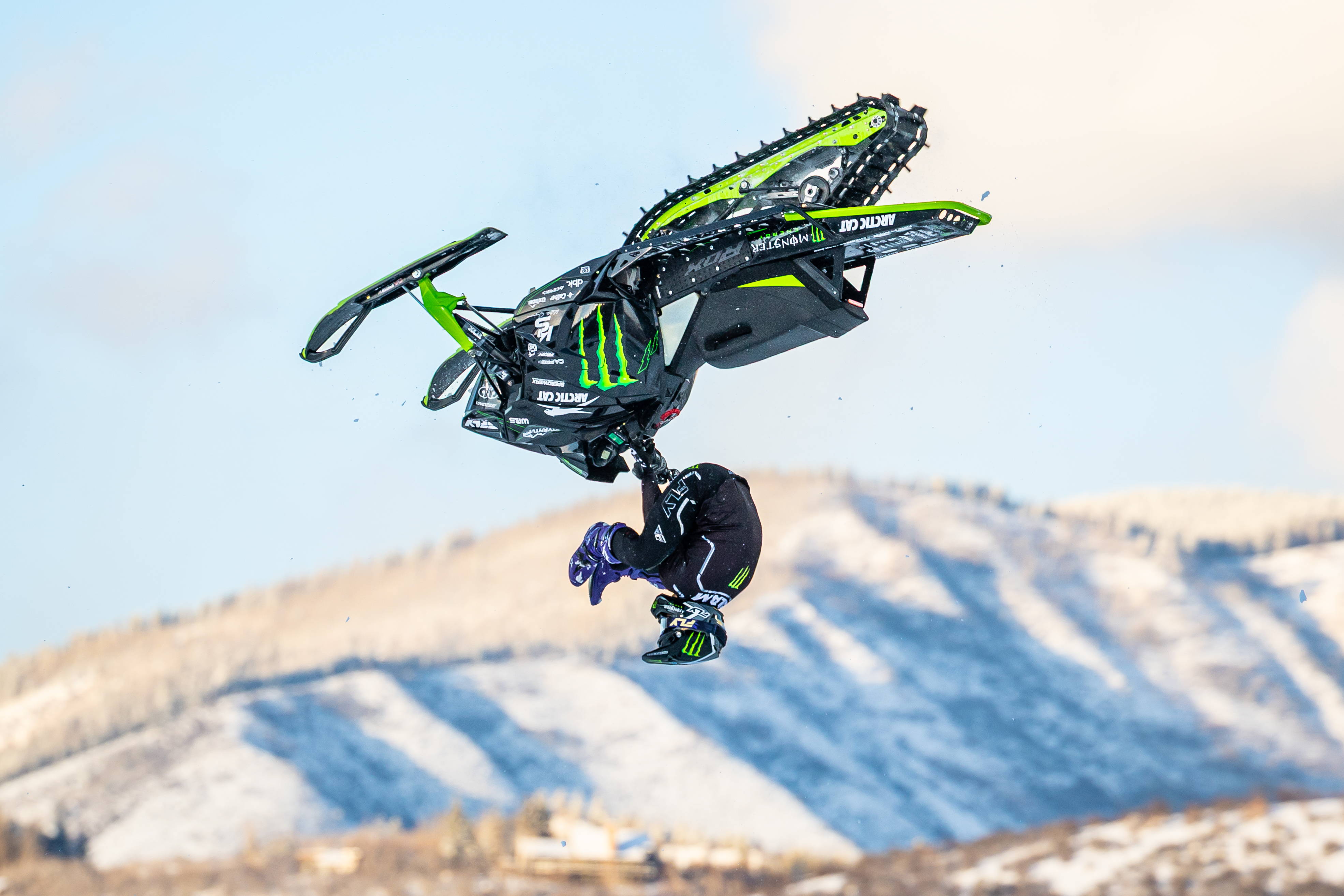 Willie Elam inverted backflip on Monster Energy Arctic Cat sled, mountains behind